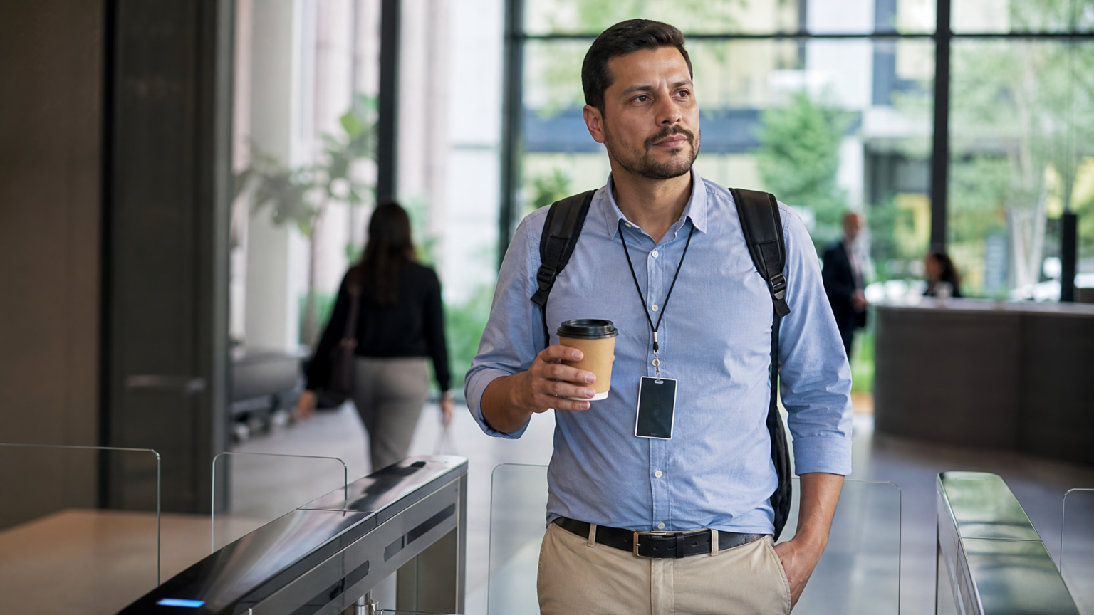 Coffee badging: quando ir ao escritório vira só prova de presença Profissional com crachá e café no escritório representando coffee badging no trabalho híbrido