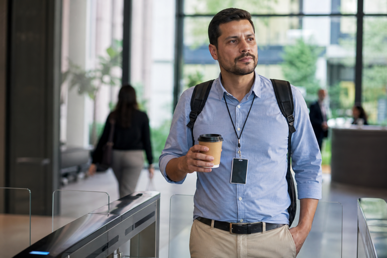 Profissional com crachá e café no escritório representando coffee badging no trabalho híbrido