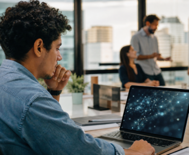 Jovem profissional diante de laptop com interface abstrata de IA em ambiente corporativo, representando IA e primeiro emprego