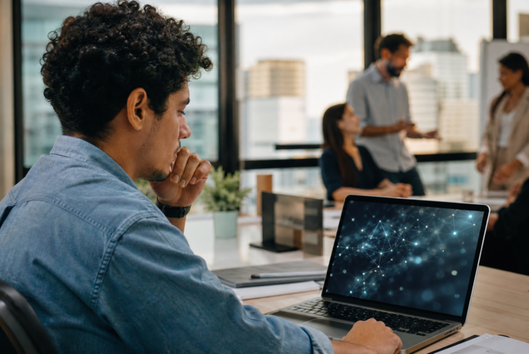 Jovem profissional diante de laptop com interface abstrata de IA em ambiente corporativo, representando IA e primeiro emprego